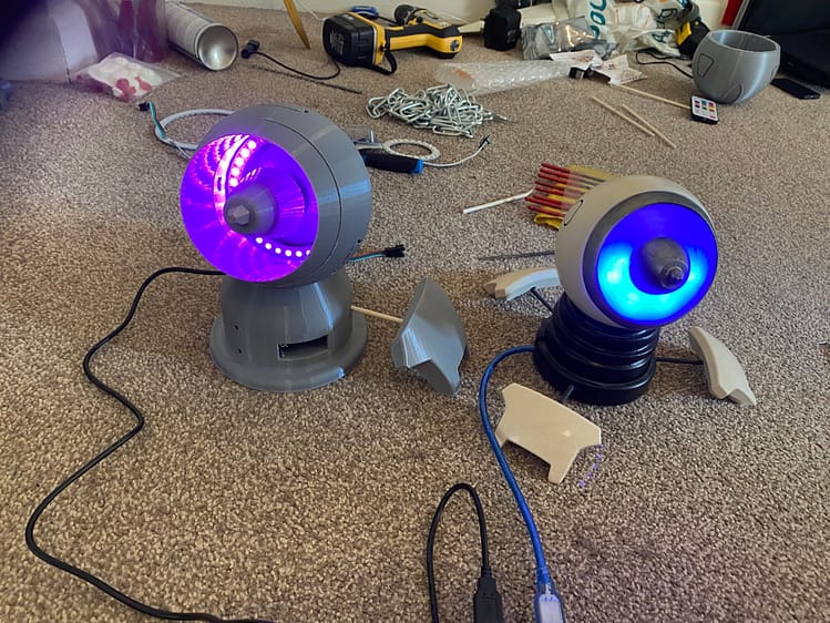 Two versions of the Symmetra turret, both lit up. Chaotic workspace in the background.