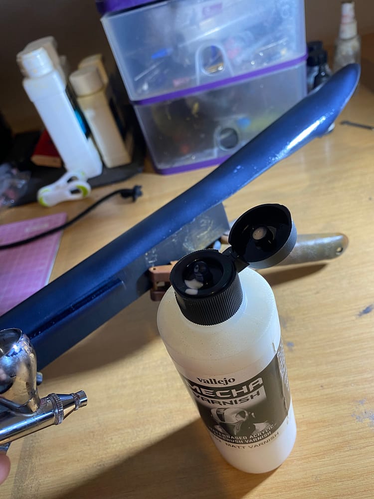 A black component with the airbrush and matt varnish next to it.