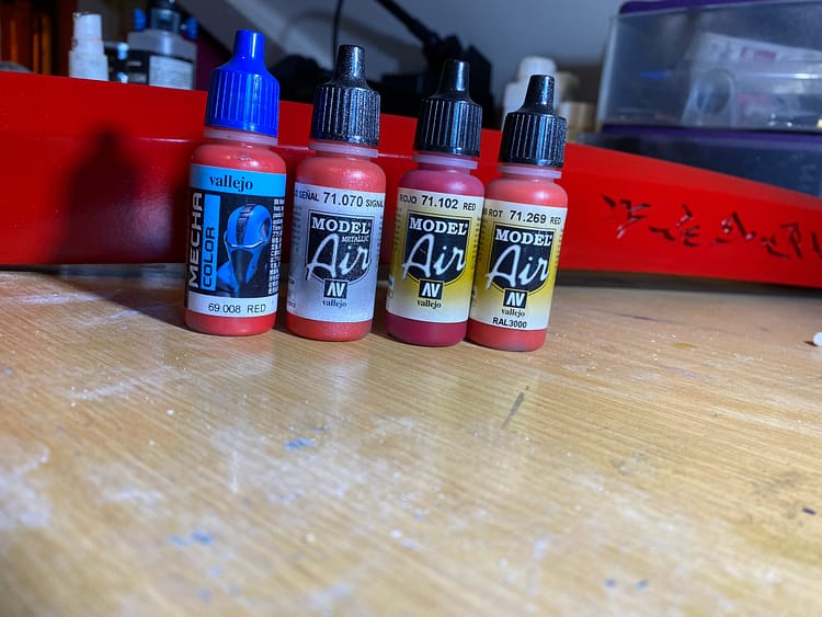 Four red airbrush paints, sitting in a line. FOUR RED AIRBRUSH PAINTS SITTING IN A LINE.